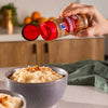 A hand sprinkles McCormick cinnamon from a spice container onto a bowl of rice pudding.