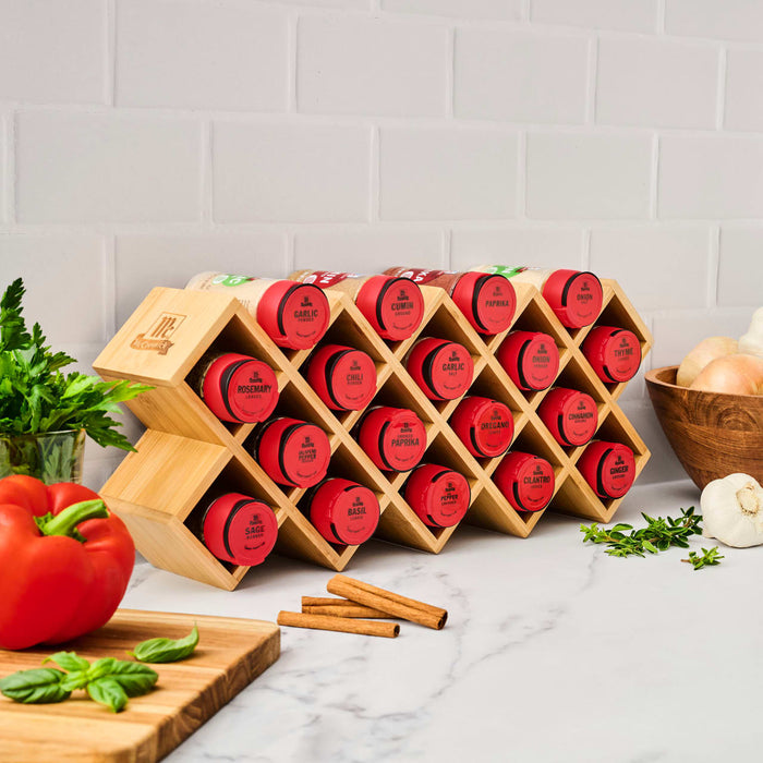 A bamboo spice rack from Gneiss Spice displays red-labeled spice jars on a kitchen counter.