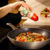 A person is adding McCormick Garlic Salt to a stir-fry in a wok.