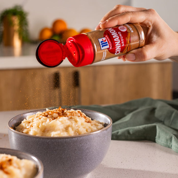 A hand sprinkles McCormick Cinnamon onto a bowl of rice pudding.