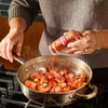 A person seasons shrimp in a pan with McCormick spices on a stovetop.