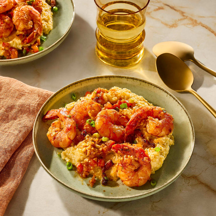 A plate of shrimp and grits is presented with a glass of white wine and gold utensils, suggesting a gourmet dining experience.