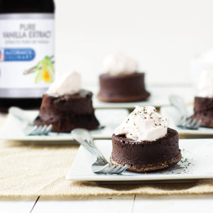 A plate of chocolate lava cakes topped with whipped cream and sprinkled with herbs.