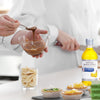 A person is pouring chocolate into a bowl while a bottle of McCormick Culinary Imitation Banana Extract sits on the table.