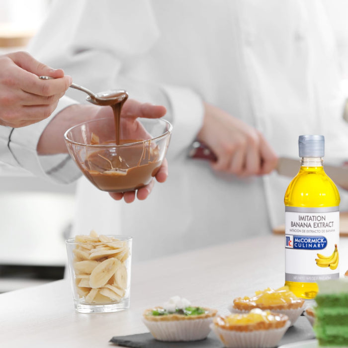 A person is pouring chocolate into a bowl while a bottle of McCormick Culinary Imitation Banana Extract sits on the table.