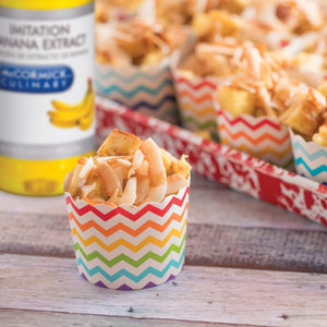 A close-up of a single serving of french toast topped with coconut flakes in a colorful cup with a bottle of McCormick Imitation Banana Extract in the background.
