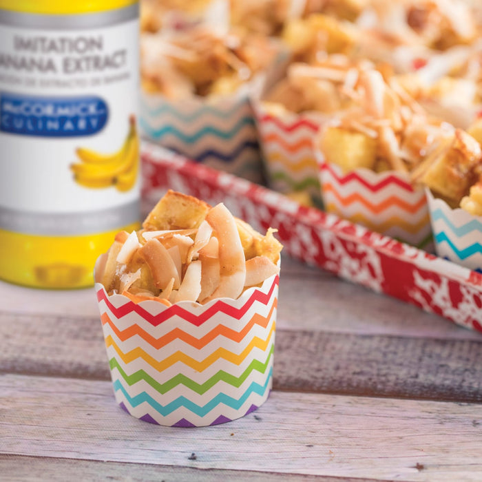 A close-up of a single serving of french toast topped with coconut flakes in a colorful cup with a bottle of McCormick Imitation Banana Extract in the background.