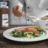A chef is pouring a creamy sauce over a plate of salmon avocado and greens.