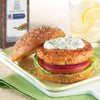 A McCormick Dill Seed spice jar is next to a salmon burger on a sesame seed bun with a creamy dill sauce tomato red onion and lettuce.