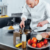 A chef is preparing a meal in a kitchen using tongs to stir a pan of food.