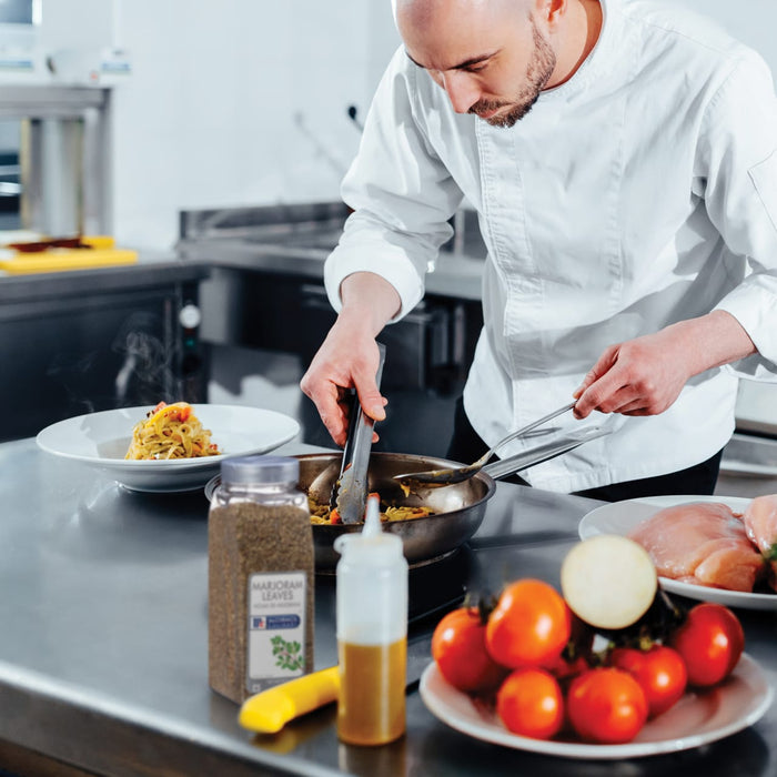 A chef is preparing a meal in a kitchen using tongs to stir a pan of food.