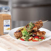 A plate of grilled steak skewers with zucchini mushrooms and tomatoes served over a bed of orzo pasta with a pesto sauce.