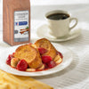 A plate of French toast with strawberries and bananas a cup of coffee and a box of McCormick Culinary Cinnamon Sugar.