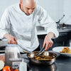 A chef in a white uniform uses tongs to stir vegetables in a pan.
