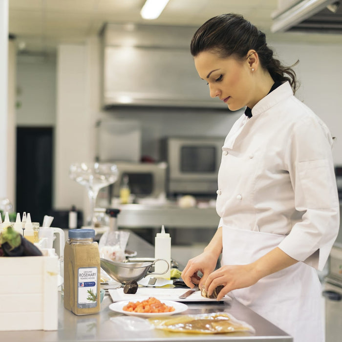 A chef in a white uniform is preparing food in a kitchen using McCormick Culinary Ground Rosemary.
