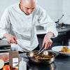 A chef in a white uniform uses tongs to stir vegetables in a pan.
