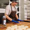 A baker wearing blue gloves rolls out dough on a wooden counter with a jar of McCormick Ground Allspice in the background.