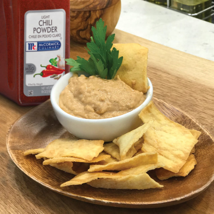 A bowl of hummus with pita chips and a jar of McCormick Culinary Light Chili Powder.