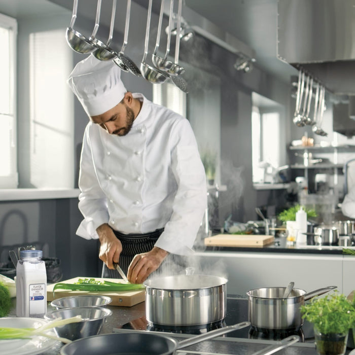 A chef in a white uniform is preparing a meal in a kitchen with a pot of boiling water on the stove and a bottle of McCormick Culinary Flavor Enhancer MSG.