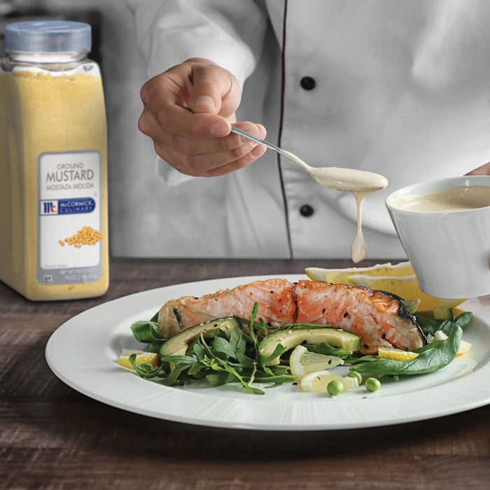 A chef is pouring a creamy sauce over a plate of salmon avocado and greens.