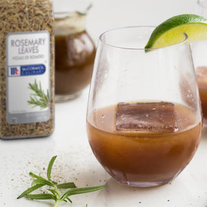 A glass of McCormick Culinary Rosemary Leaves infused cocktail with a lime wedge and ice.