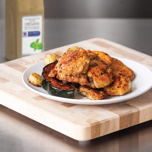A plate of roasted chicken squash and potatoes sits on a wooden cutting board.