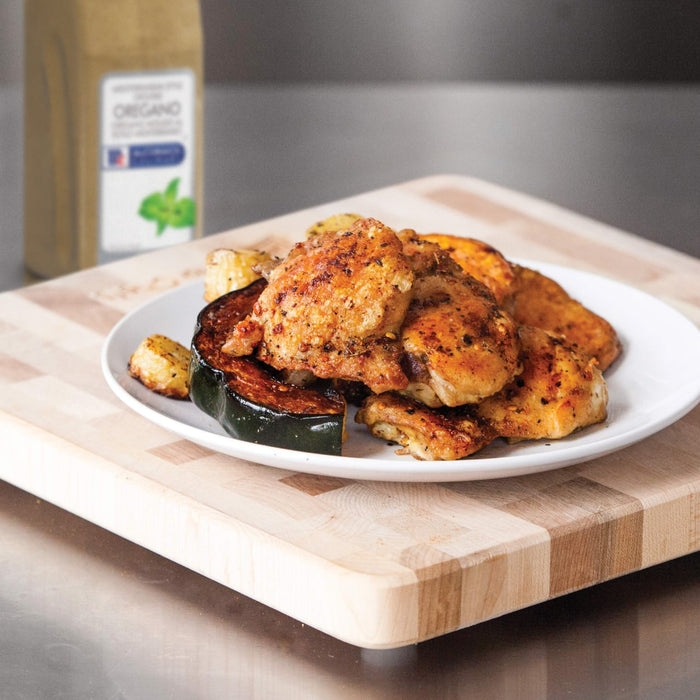 A plate of roasted chicken squash and potatoes sits on a wooden cutting board.