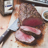 A close-up of a sliced roast beef seasoned with McCormick Culinary Cracked Black Pepper on a wooden cutting board.