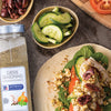 A bottle of McCormick Culinary Greek Seasoning next to a pita bread filled with chicken tomatoes cucumbers spinach feta cheese and olives.