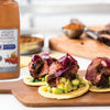 Three tacos with grilled steak red onion and guacamole on a wooden cutting board with McCormick Culinary Mesquite Barbecue Seasoning.