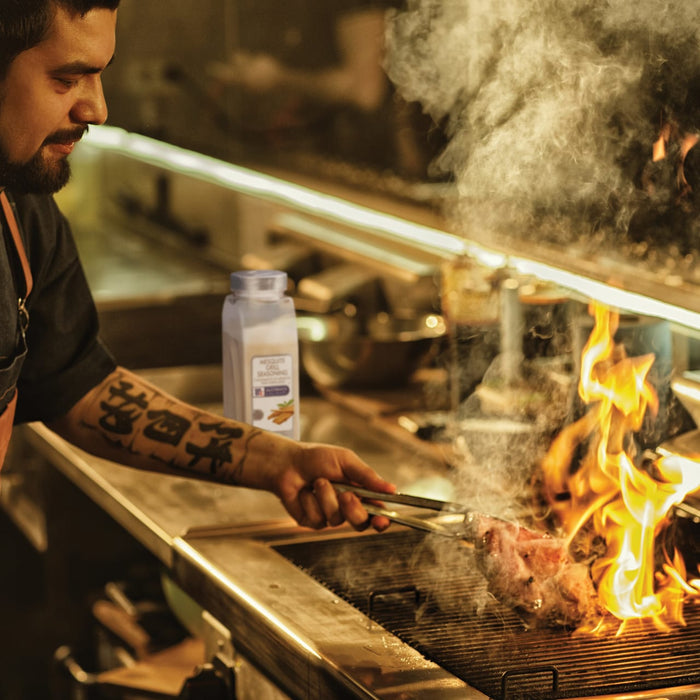 A chef uses a pair of tongs to flip a piece of meat on a hot grill with a bottle of McCormick Grill Mating in the background.