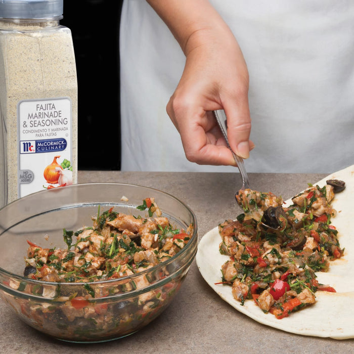 A hand is using a spoon to add a McCormick Culinary Fajita Marinade &amp; Seasoning to a tortilla.