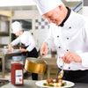 A chef is plating a dish of meat and vegetables using a spoon to drizzle sauce over the top with a jar of McCormick Culinary Ground Chipotle Chile Pepper in the foreground.