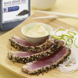 Seared tuna topped with black sesame seeds served with a side of white noodles and a small bowl of mayonnaise.