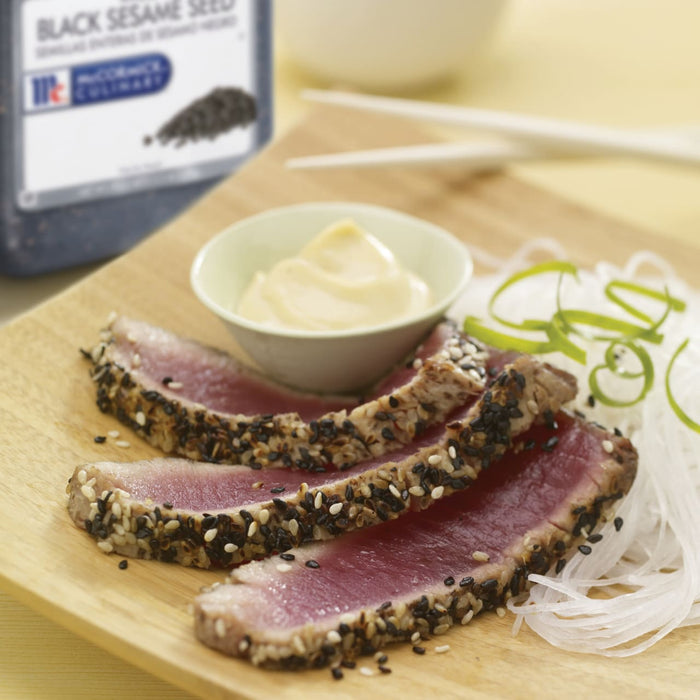 Seared tuna topped with black sesame seeds served with a side of white noodles and a small bowl of mayonnaise.