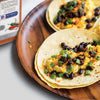 A close-up of a taco filled with black beans scrambled eggs and green onions on a wooden plate with a McCormick Southwest Seasoning jar in the background.