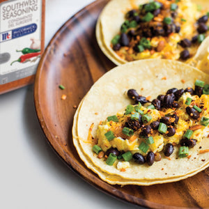 A close-up of a taco filled with black beans scrambled eggs and green onions on a wooden plate with a McCormick Southwest Seasoning jar in the background.