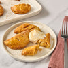 A plate of golden-brown apple hand pies is served with a dollop of cream, showcasing a delicious dessert option.