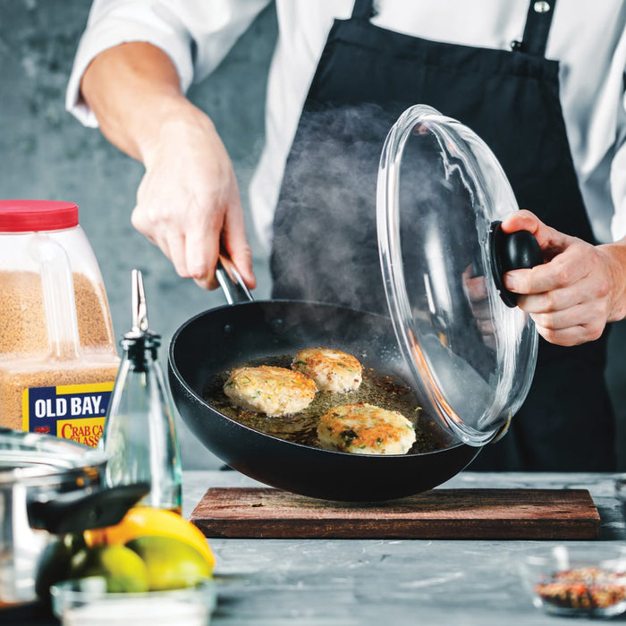 A chef is cooking crab cakes in a pan with Old Bay seasoning.