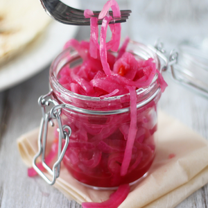 A jar of pickled red onions with a fork holding some of the onions.