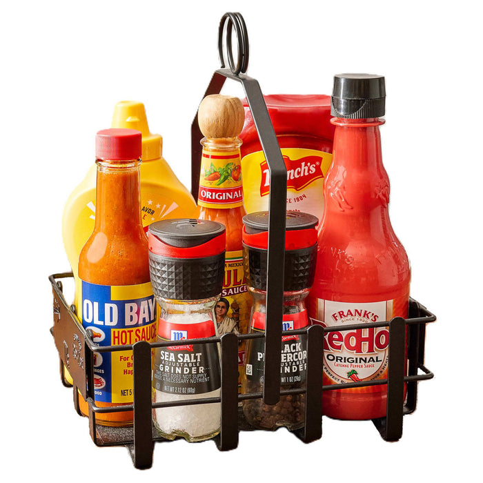 A black metal condiment caddy holds a variety of flavor enhancers including Old Bay Hot Sauce, McCormick Sea Salt Grinder, McCormick Black Peppercorn Grinder, Frank's RedHot Original Cayenne Pepper Sauce, Cholula Original Hot Sauce, and French's Mustard.