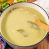 A pot of creamy green soup with bay leaves and a wooden spoon.