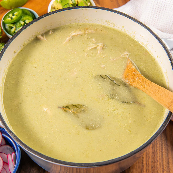 A pot of creamy green soup with bay leaves and a wooden spoon.