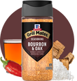 Bottle of McCormick Grill Mates Bourbon & Oak seasoning with a glass of bourbon, red pepper, and wood chips on a white background.