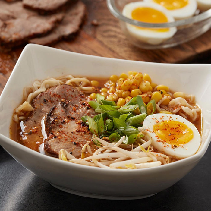 A bowl of ramen with pork, corn, bean sprouts, green onions, and a soft boiled egg.