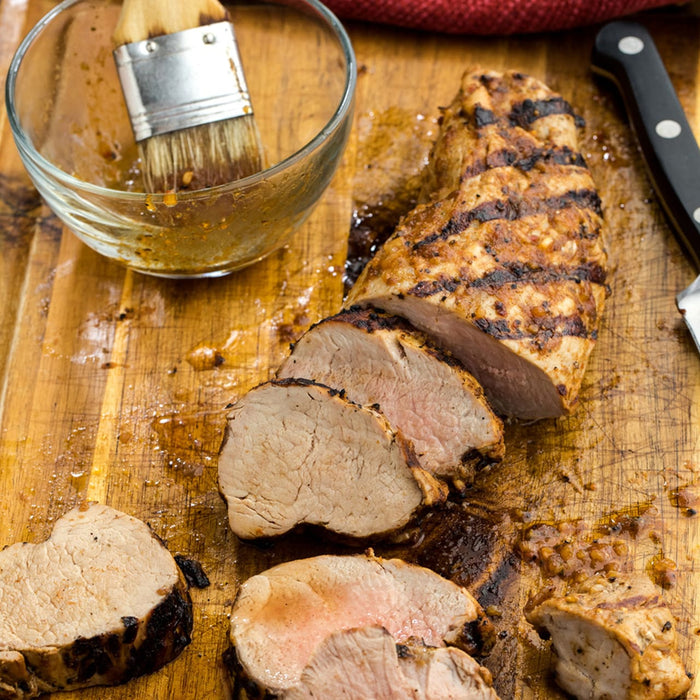 Grilled pork tenderloin sliced on a wooden cutting board.