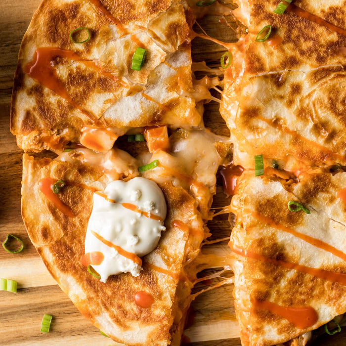 A close-up of a buffalo chicken quesadilla with melted cheese and a side of ranch dressing.