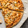 A close up view of several slices of buffalo chicken pizza topped with chunks of chicken and drizzled with ranch dressing on parchment paper.
