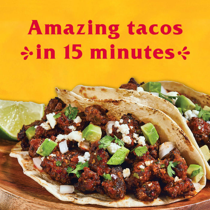 Two tacos filled with meat avocado cilantro and cheese on a wooden cutting board.