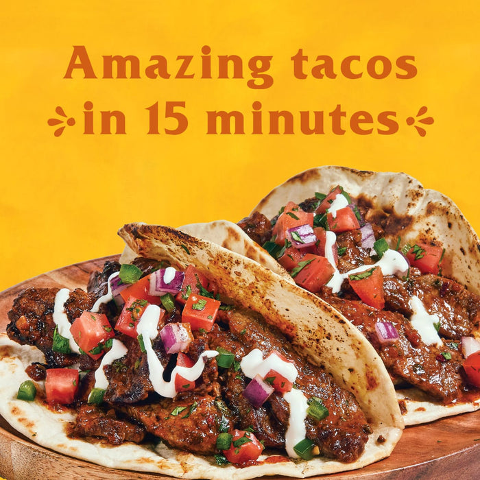 Two tacos filled with meat tomatoes onions and sour cream on a wooden plate.